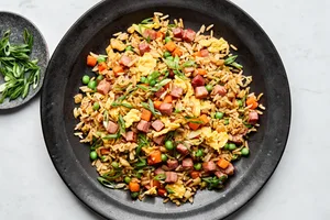 A bowl of ham fried rice, featuring fluffy rice mixed with diced ham, scrambled egg, peas & carrots, topped with green onions