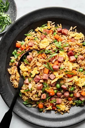 A bowl of ham fried rice, featuring fluffy rice mixed with diced ham, scrambled egg, peas & carrots, topped with green onions