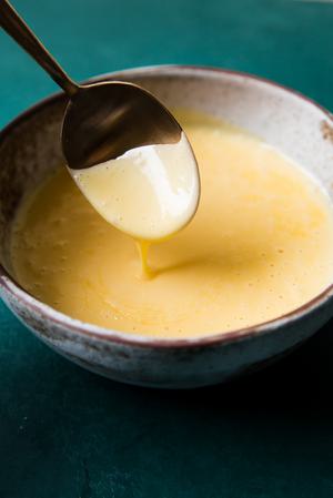 a spoon scooping homemade hollandaise sauce out of a bowl