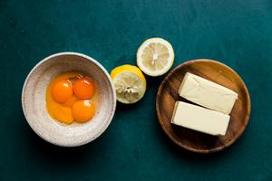 Ingredients laid out for homemade hollandaise sauce: two sticks of butter, lemon juiced and egg yolks in a bowl