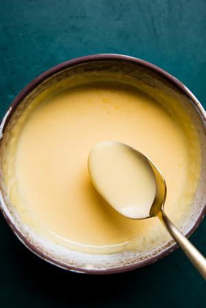 a spoon scooping homemade hollandaise sauce out of a bowl