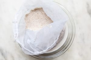 blended soaked almonds, water, vanilla, cinnamon, and dates in a nut bag sitting in a glass bowl