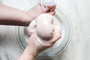 blended soaked almonds, water, vanilla, cinnamon, and dates in a nut bag being squeezed into a glass bowl