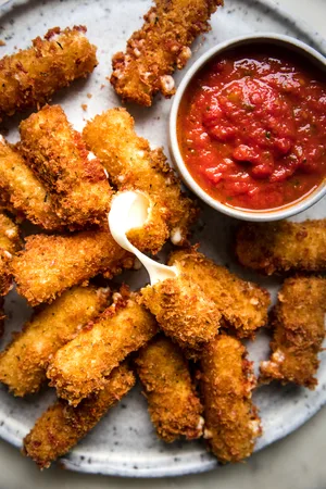 homemade mozarella sticks on a platter wit a bowl of marinara dipping sauce