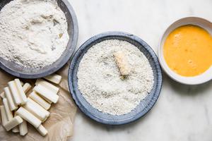 mozarella cheese sticks beside bowls of flour, panko and eggs for homemade mozzarella sticks