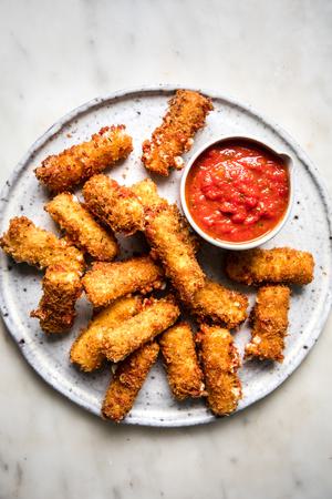 homemade mozarella sticks on a platter wit a bowl of marinara dipping sauce