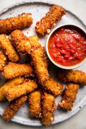 homemade mozarella sticks on a platter wit a bowl of marinara dipping sauce