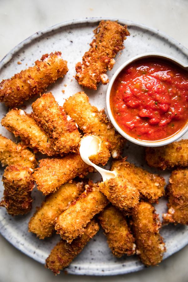 homemade mozarella sticks on a platter with a bowl of marinara dipping sauce