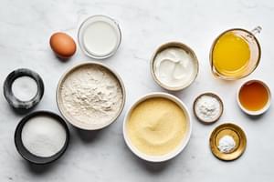cornmeal, flour, baking powder, baking soda, salt, butter, sugar, honey, eggs, sour cream and milk in prep bowls