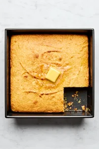 homemade cornbread in a 9x9 baking dish with a slice cut out topped with a pat of butter