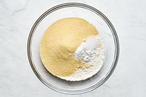 cornmeal, flour, baking powder, baking soda, and salt being combined in a bowl