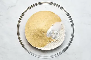 cornmeal, flour, baking powder, baking soda, and salt being combined in a bowl