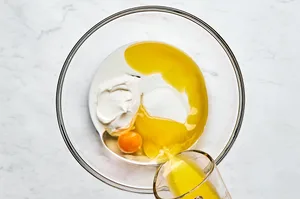 melted butter, sugar, honey, egg, sour cream, and milk being mixed in a bowl