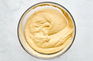 melted butter, sugar, honey, egg, sour cream, and milk being mixed with flour, cornmeal, baking powder & soda and salt