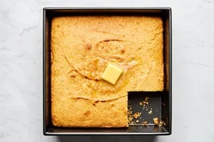 homemade cornbread in a 9x9 baking dish with a slice cut out topped with a pat of butter