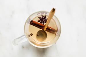 a cinnamon stick, anise, cloves, hot water, honey, lemon juice, bitters and bourbon in a mug with a spoon