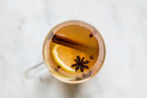 a homemade hot toddy in a mug with cinnamon stick, clove, anise and a lemons lice for garnish