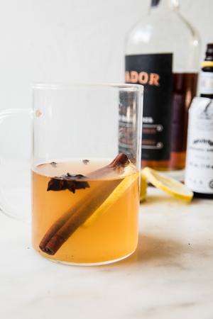 a homemade hot toddy in a mug with cinnamon stick, clove, anise and a lemons lice for garnish