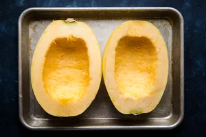 a spaghetti squash cut in half with the seeds scraped out on a baking sheet