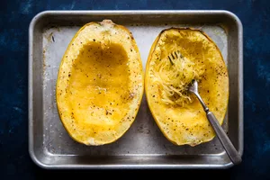 oven roasted spaghetti squash seasoned with salt and pepper on a baking sheet being shredded with a fork