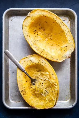 Cooked spaghetti squash with salt and pepper being shredded into strands showing you how to cook a spaghetti squash