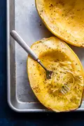 Cooked spaghetti squash with salt and pepper being shredded into strands showing you how to cook a spaghetti squash