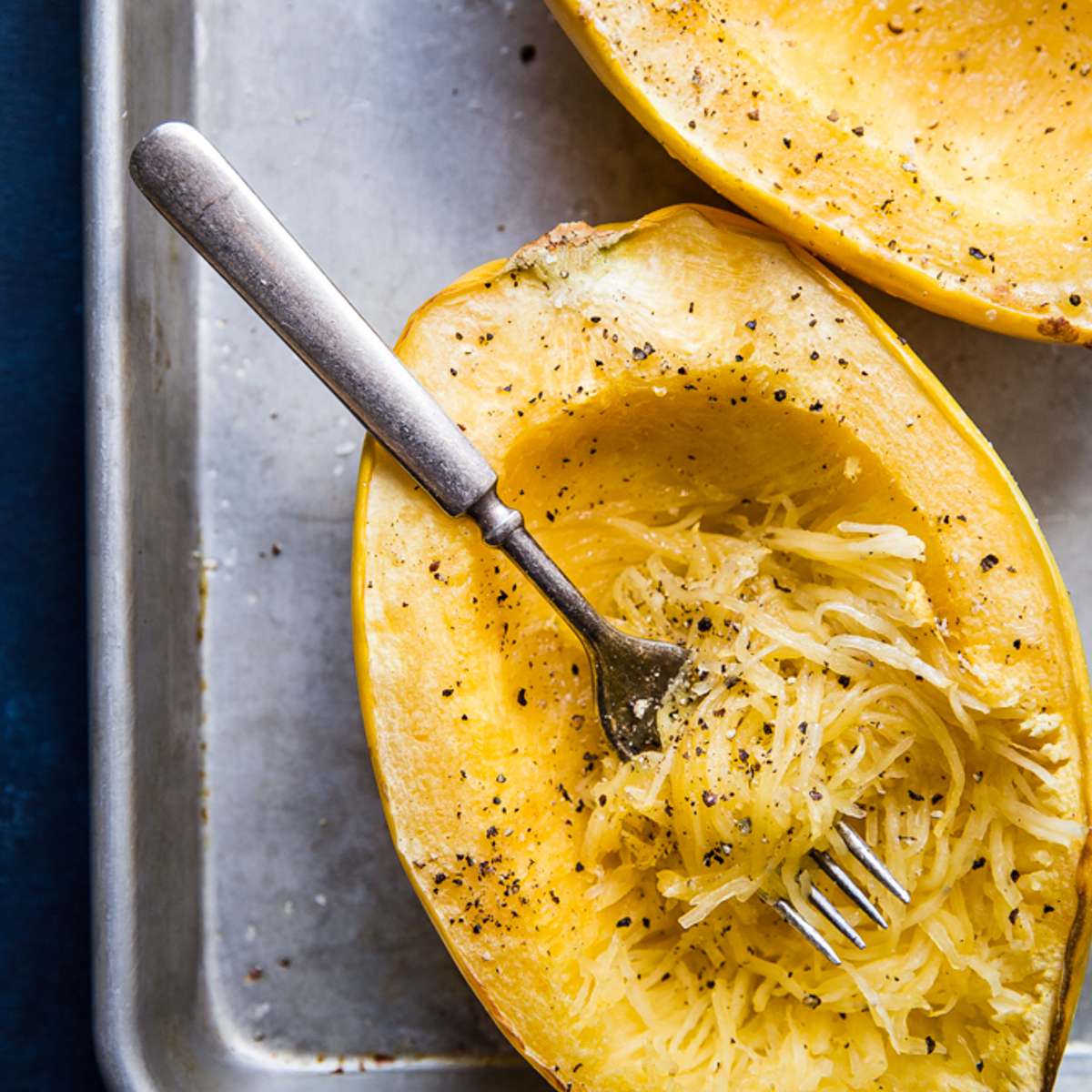 Cooked spaghetti squash with salt and pepper being shredded into strands showing you how to cook a spaghetti squash