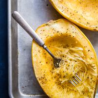 Cooked spaghetti squash with salt and pepper being shredded into strands showing you how to cook a spaghetti squash