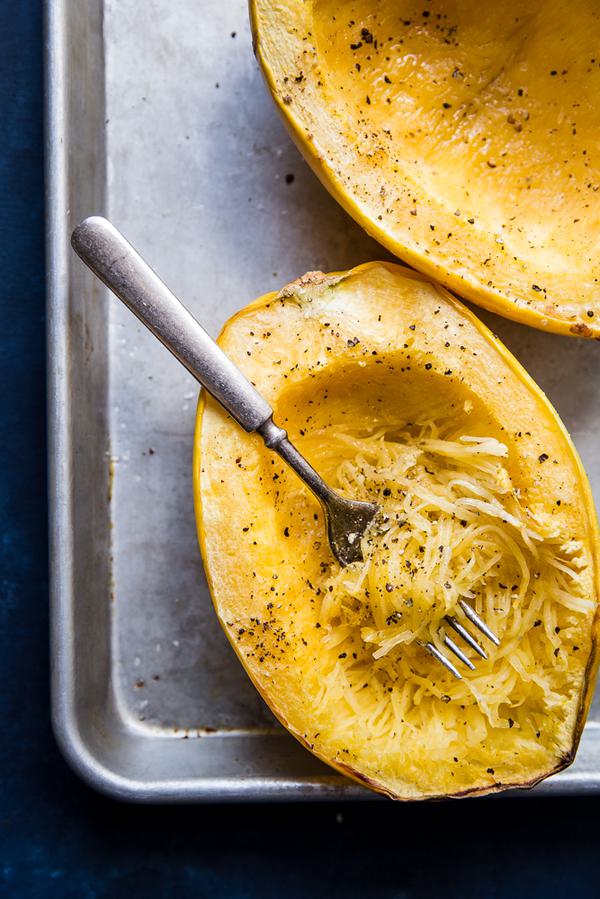 Cooked spaghetti squash with salt and pepper being shredded into strands showing you how to cook a spaghetti squash