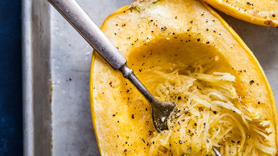 Cooked spaghetti squash with salt and pepper being shredded into strands showing you how to cook a spaghetti squash
