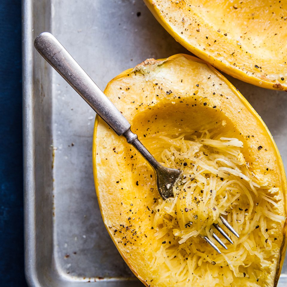 Cooked spaghetti squash with salt and pepper being shredded into strands showing you how to cook a spaghetti squash