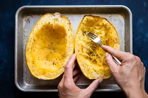 oven roasted spaghetti squash with salt and pepper on a baking sheet with hands using a fork to scrape some out