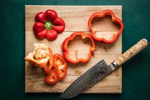 bell peppers with tops and bottoms cut off and cut into 2 rings on a cutting board with a knife