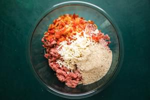 ground beef, sausage, bell peppers, garlic and cheese for stuffed peppers in a mixing bowl