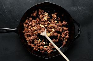 ground Italian sausage being cooked in a frying pan with a wooden spoon
