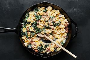 orecchiette pasta with sausage and kale in a large black skillet with a wooden spoon