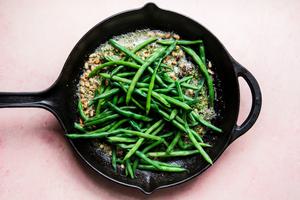 pine nuts, pesto, butter and green beans cooking in a skillet