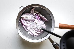 boiling water being poured over sliced red onions in a mesh strainer