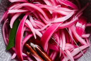 Pickled red onions in a bowl, vibrant and tangy, perfect for adding flavor to tacos, sandwiches, or salads.