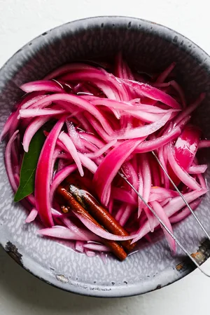 Pickled red onions in a bowl, vibrant and tangy, perfect for adding flavor to tacos, sandwiches, or salads.