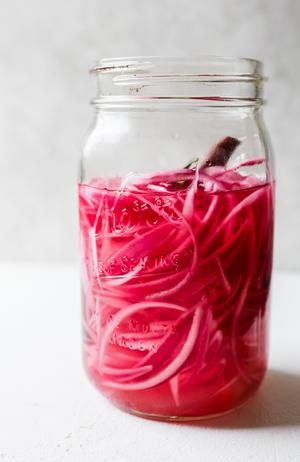 a jar of pickled red onions in a bowl, vibrant and tangy, perfect for adding flavor to tacos, sandwiches, or salads.