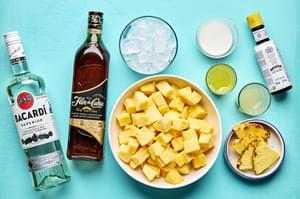 frozen pineapple, ice, cream of coconut, pineapple juice, lime juice, rum and angostura laid out to make piña coladas