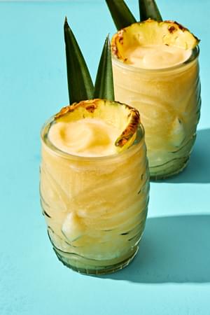 Homemade piña colada served in a tiki glass, topped with a slice of pineapple and pineapple leaves for garnish.