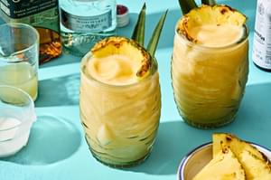 Homemade piña colada served in a tiki glass, topped with a slice of pineapple and pineapple leaves for garnish.