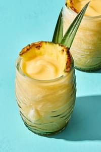 Homemade piña colada served in a tiki glass, topped with a slice of pineapple and pineapple leaves for garnish.