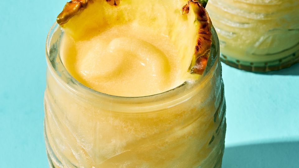 Homemade piña colada served in a tiki glass, topped with a slice of pineapple and pineapple leaves for garnish.