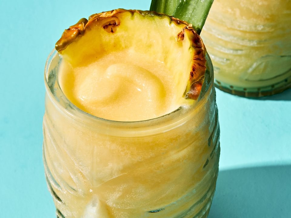 Homemade piña colada served in a tiki glass, topped with a slice of pineapple and pineapple leaves for garnish.