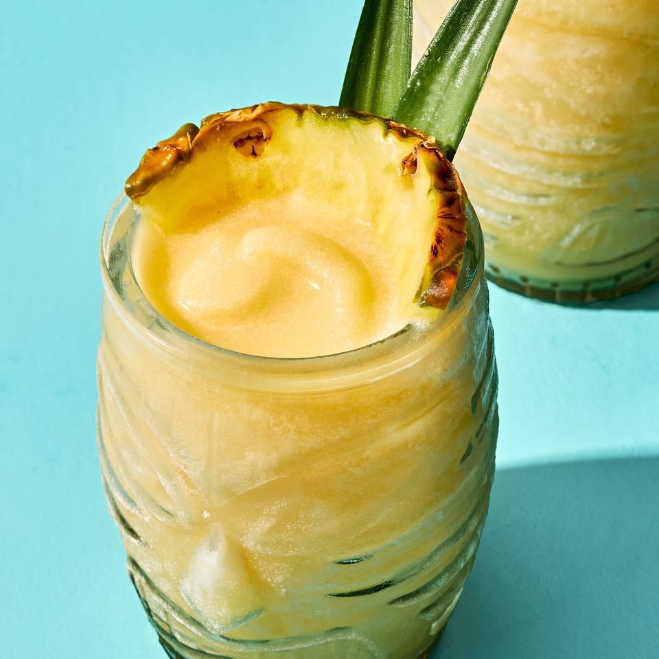 Homemade piña colada served in a tiki glass, topped with a slice of pineapple and pineapple leaves for garnish.