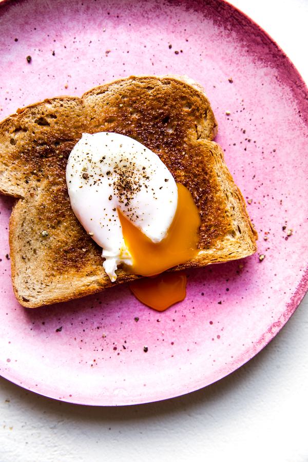 Pink plate with a piece of toast and a poached egg with salt and pepper