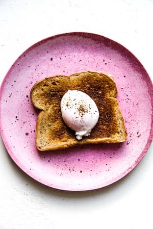 Pink plate with a piece of toast and a poached egg with salt and pepper